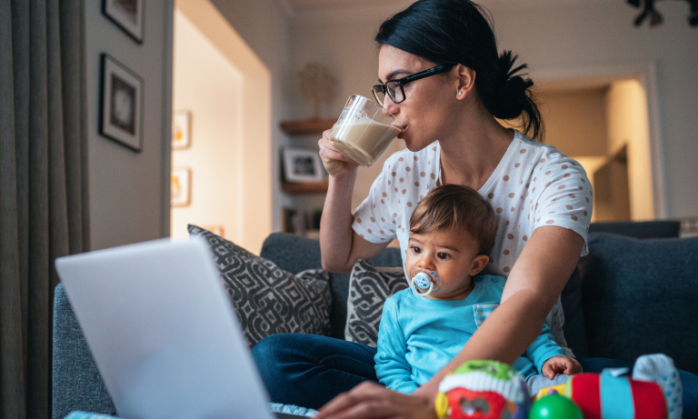 A mother sitting at her computer, drinking coffee with a child in her lap